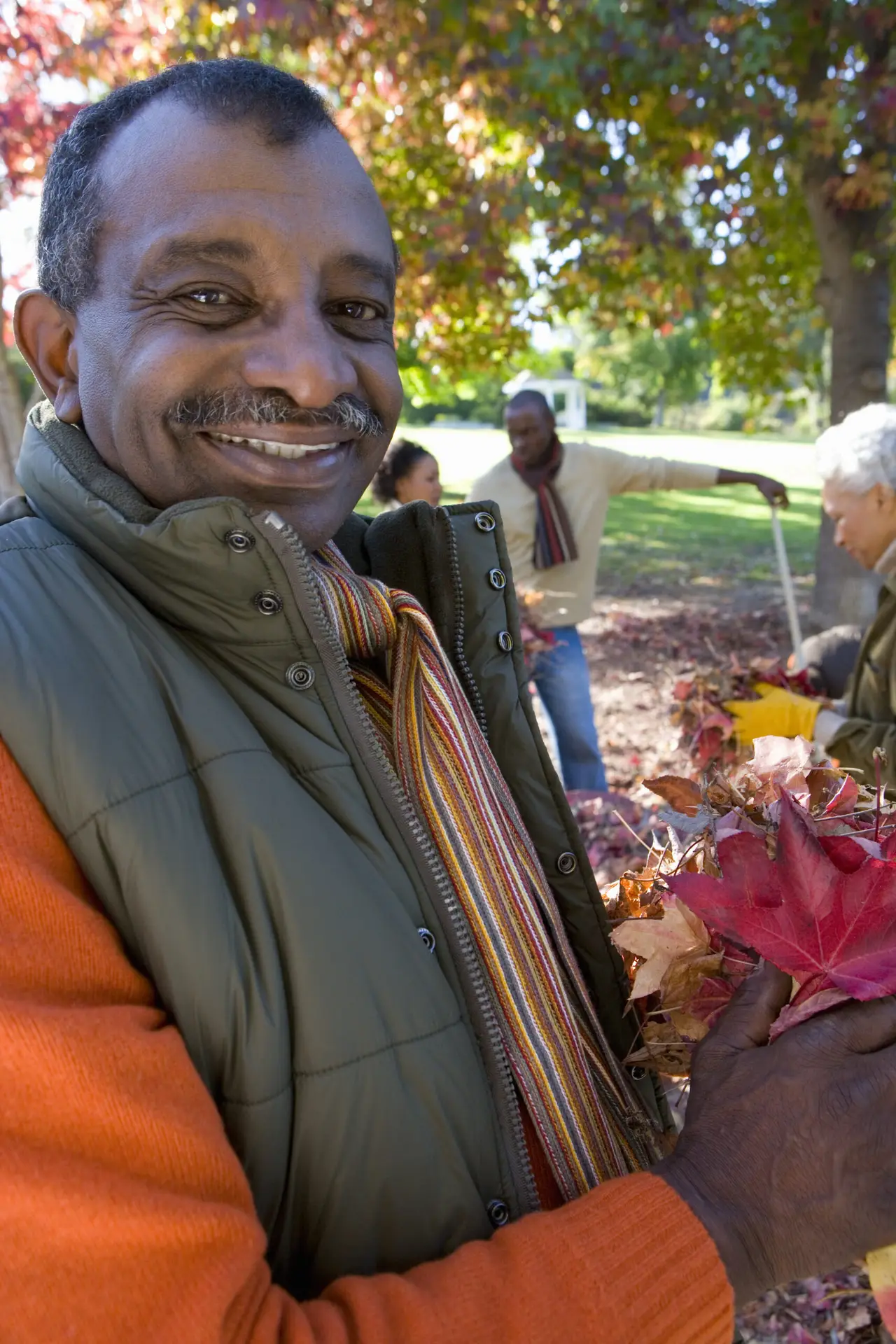 Man smiling outdoors while holding colorful autumn leaves